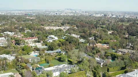 Aerial pullback shot of Beverly Hills residences, green foliage, and LA skyline Stock Footage 272496381