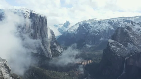 Aerial pullback shot of Yosemite snow mountains and cliffs through clouds Stock Footage 270958500