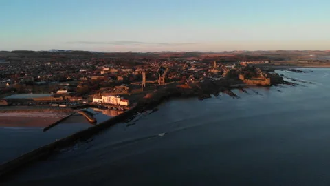 Aerial pullback of St Andrews town from ocean during sunrise in winter Stock Footage 147396115