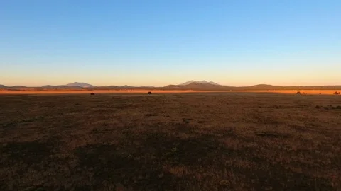 Aerial pullback of a vast prairie with distant mountain peaks and an old cabin Видео 81104661