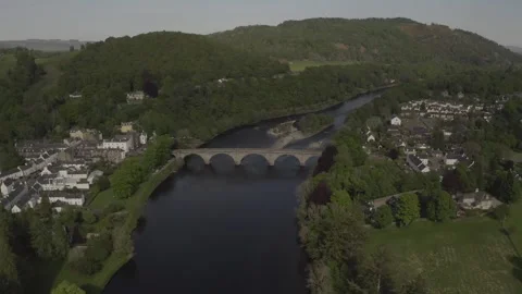 Aerial pullback view of Dunkeld town, old arched bridge crossing River Tay and Vídeos de archivo 251033877