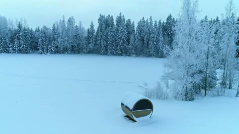 Aerial pullback Wooden barrel sauna on Snow covered meadow, Frost forest Stock Footage 219624713