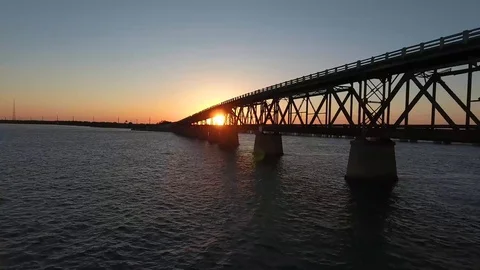 AERIAL: Pulling back from an old broken down bridge at sunset over the Stock Footage 98669324