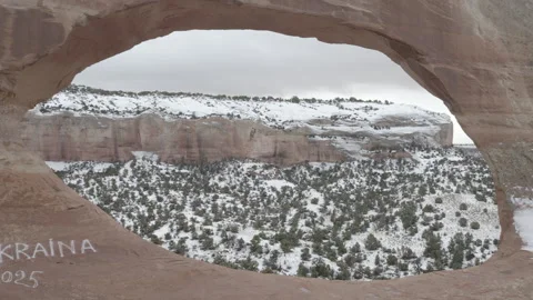 Aerial pulls back from mountain range through Wilson Arch on snowy morning Видео 303396539