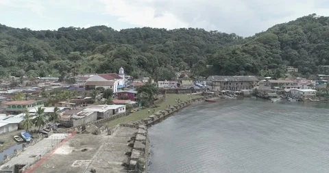 Aerial pulls back from the Portobelo fort to reveal a boat leaving the bay Stock Footage 99851355