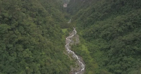 Aerial pulls back from a river to reveal green mountains leading to a valley Vídeos de archivo 80657380