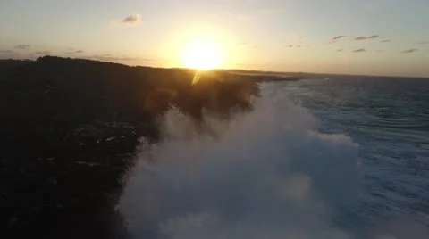Aerial pulls back from sunset as waves crash up high in front of the lens Vídeos de archivo 65407808