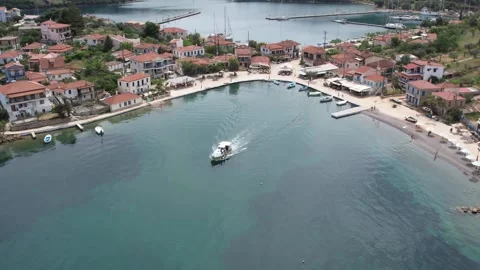 Aerial push out shot of boat leaving peaceful Greek island harbor Stock Footage 343944375