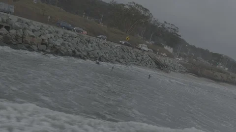Aerial push roll and pan along rocky coastline with surfers Stock Footage 107421462
