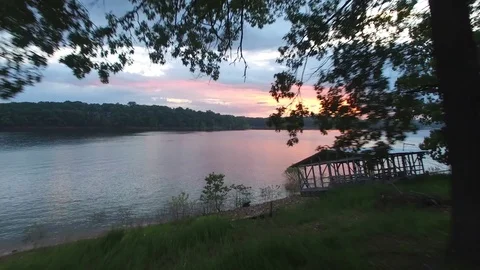 Aerial push through trees revealing sunset over a lake Stock Footage 77698459