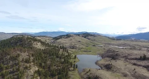 Aerial push towards small mountain lake with hills, trees, mountains in b/g Stock Footage 88454775