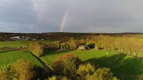Aerial of rainbow flying upwards above rural landscape meadow and pasture Stock Footage 75242567