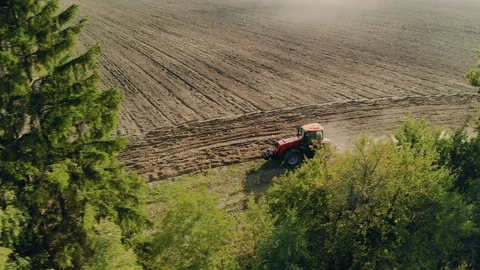 Aerial: a red working tractor with a plow behind the roadside plantings Stock Footage 123064574