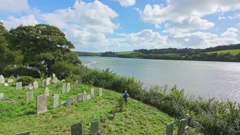 Aerial reveal of a man stood in a graveyard and Fowey river in Cornwall Video stock 345006007