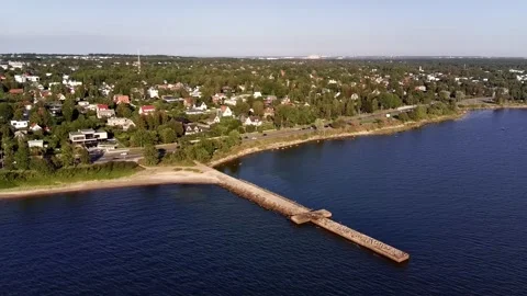 Aerial reverse orbit of coastal town and stone pier with TV tower in background Stock Footage 344759540