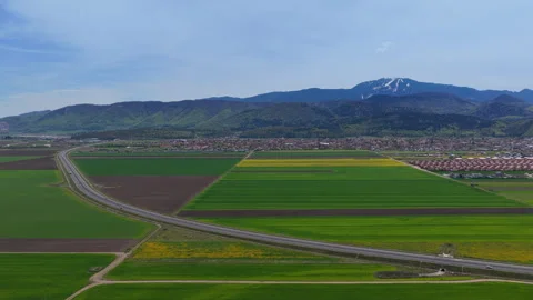 Aerial right pan of highway through green fields and snowy mountains Stock Footage 337466432