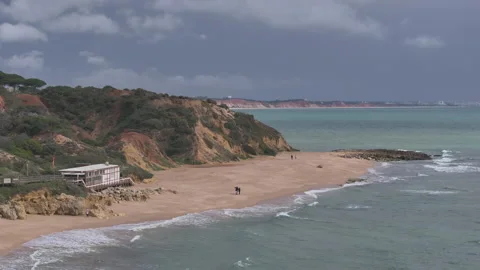 Aerial rise over red cliffs and beach in Albufeira under cloudy sky Stock Footage 346651672