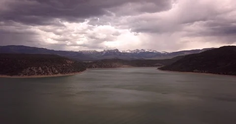 Aerial rising above a lake with dramatic storm clouds and snow capped mountains Stock Footage 99569583