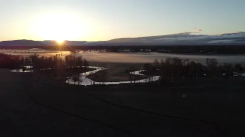 Aerial Rising Above Patch of Trees to Reveal Rising Sun Over Mountains and Creek 스톡 동영상 196949928