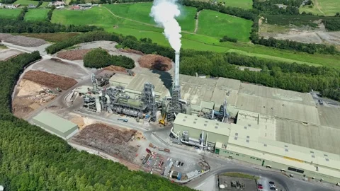 Aerial rising wood processing plant with steam from chimney and log stock piles 库存影片 339913437