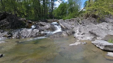 Aerial riverfront and bed flight close to the water through rocks and trees,  Stock Footage 98611953