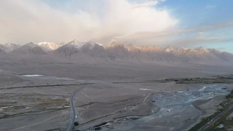 Aerial road through dry river plain below snow mountains in Xinjiang Stock Footage 337836193