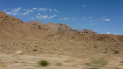 An aerial of a rocky desert vista backed by colourful mountains and blue sky. Stock Footage