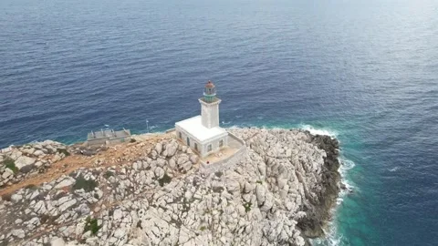 Aerial rotating shot of cliffside lighthouse above crashing ocean waves Stock Footage 338103807