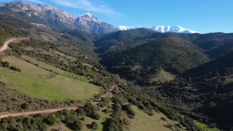 Aerial rotating view of deep valley with dirt road and snowy mountains Video stock 337459431