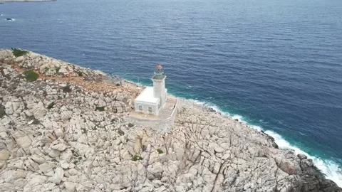 Aerial rotating view of white stone lighthouse on rocky Mediterranean cape Stock Footage 343944180