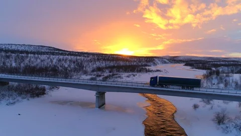 AERIAL: Semi truck crossing the bridge above icy river in the winter at sunset Stock Footage