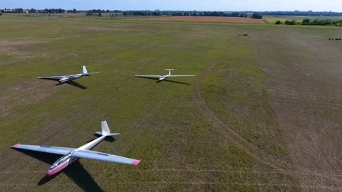 Aerial shooting of three glider planes in an even green field in a sunny day Stock Footage 81545663