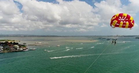 Aerial shot of 2 persons under a parasail getting towed by a boat Stock Footage 79821465
