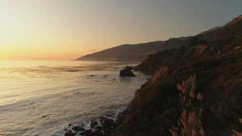 Aerial shot approaching ocean waves at sunset by a rocky coast. Orange glow. 库存影片 87645848