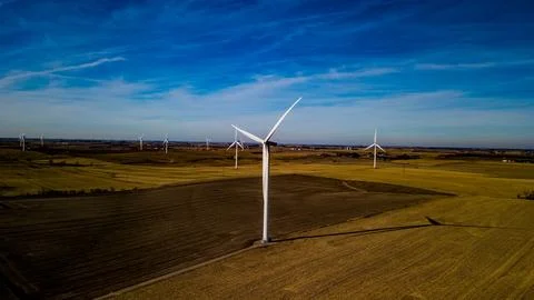 Aerial shot of an array of wind turbines standing in a lush countryside field. Stock Photos