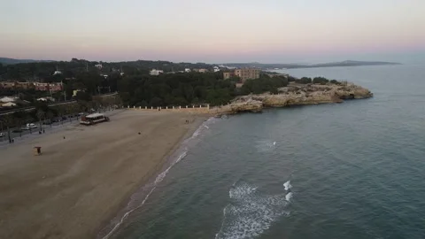 Aerial shot of a beach at sunset next to a beach bar and a rock cliff. 스톡 동영상 176563992
