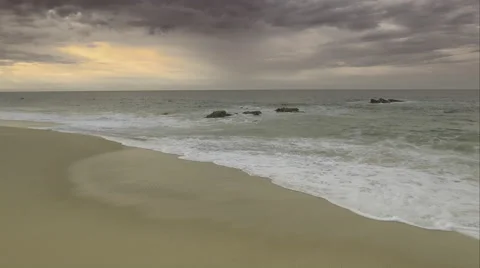 Aerial shot of a beach with waves hitting the short and rocks submerged in water Vidéo 67595956