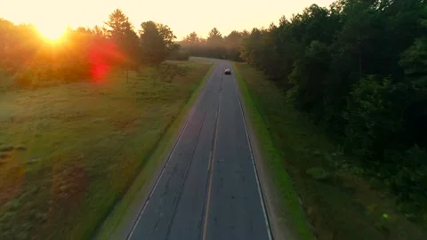 Aerial shot of car driving down country road at sunrise through foggy forests. Stock Footage 135695000