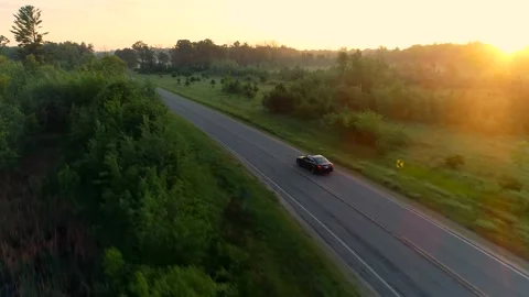 Aerial shot of car driving down country road at sunrise through foggy forests. Stock Footage