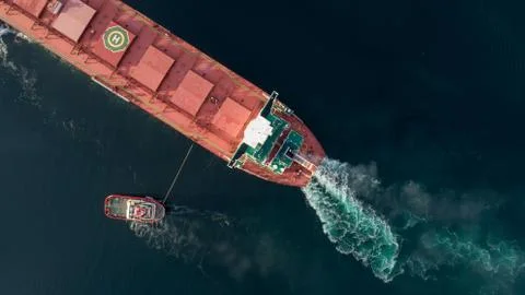 Aerial shot of a cargo ship approaching port with help of towing ship Stock Photos