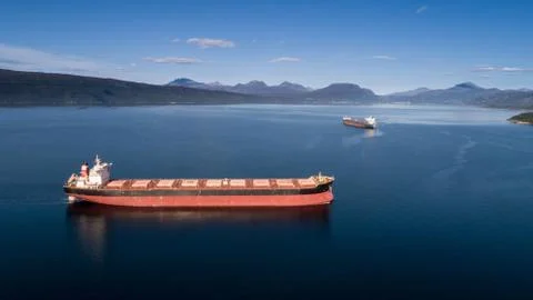 Aerial shot of a cargo ship on the open sea with other ship and mountains in  Stock Photos