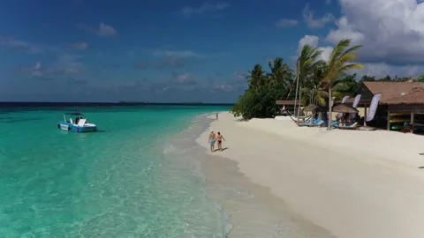 Aerial shot of a couple walking on beach of a private island luxury resort Stock Footage