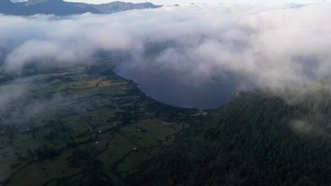 Aerial shot descending from the clouds down to a village by a lake. Stock Footage 299627584