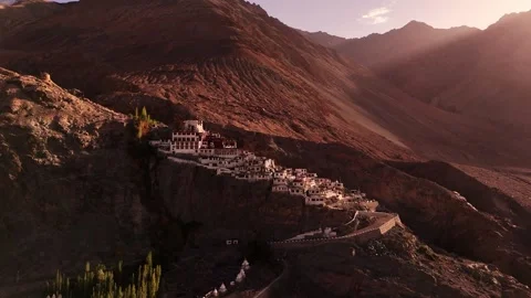 Aerial shot of Diskit Monastery glowing in golden light amidst harsh cliffs. Stock Footage 310900475