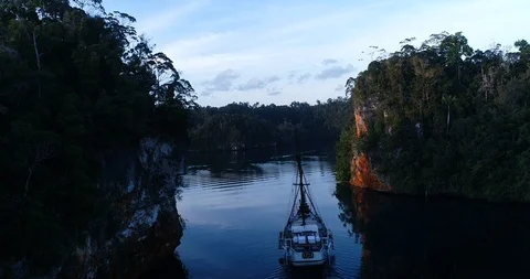 Aerial shot of diving boat navigating between rocky islands at sunrise Stock-Footage 100384036