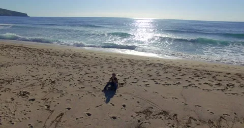 Aerial shot with drone of man thinking sitting on beach in front of ocean Stock Footage 56506069