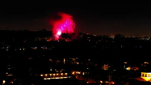Aerial Shot Of Fireworks Exploding Over Buildings In Suburb, Drone Flying Stock Footage 243880035