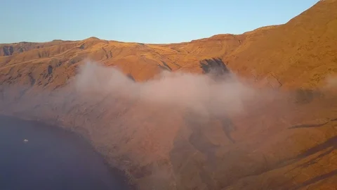 Aerial shot of fluffy clouds moving across rocky mountains at sunrise Видео 115847181
