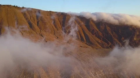 Aerial shot of fluffy clouds moving above rocky mountains during sunrise Stock Footage 115847702
