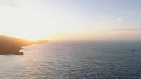 Aerial shot flying backwards over ocean, coastline and sunset on the left. Video stock 112714931